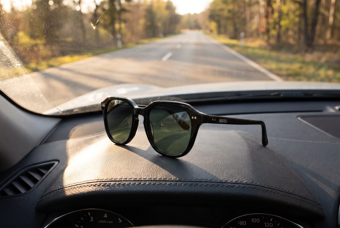 SESTO. ELIO Sonnenbrille mit grüngrauen Gläsern auf dem Armaturenbrett, Strasse im Gegenlicht